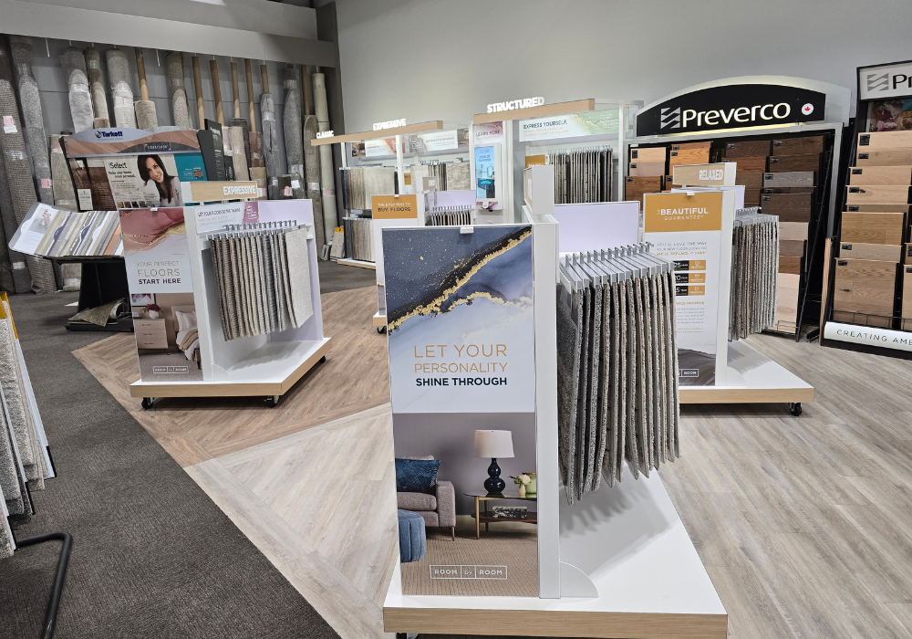 Showroom display with multiple standing tile or flooring samples on white racks, a central brochure stand reading “LET YOUR PERSONALITY SHINE THROUGH,” and brands including “Preverco.”